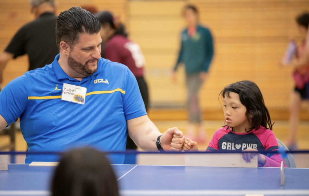 Michael Garafola (Adaptive Program Coordinator) gives a fist bump to a young girl after scoring a point during Takkyu Volley.